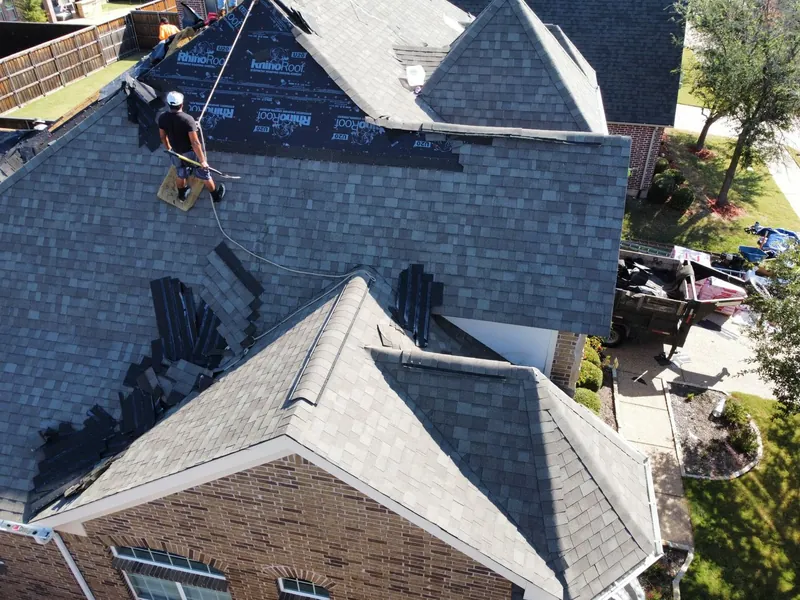 Roofer on a steep gray shingle roof installing shingles on a brick two-story home