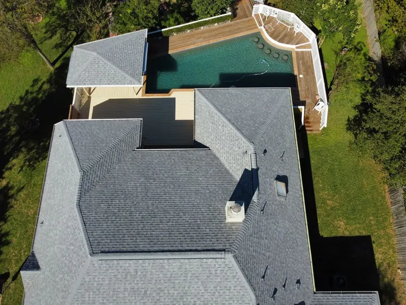 Drone view of a finished gray shingle roof on a home with a backyard pool